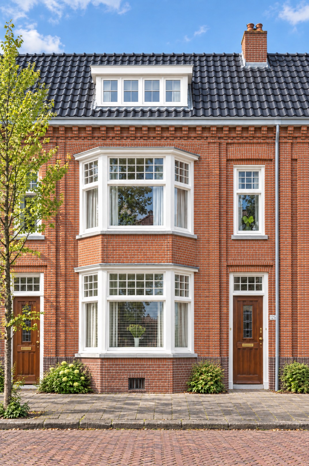 Rijwoning aan de Valeriusstraat in rode Amsterdamse baksteen, met twee erkers boven elkaar, een bruine voordeur en een pannendak